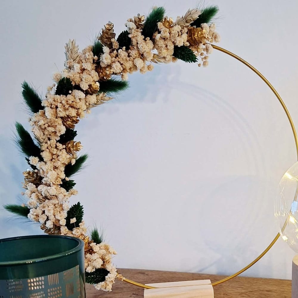Couronne de fleurs séchées crème, dorées et vert sapin sur cerceau doré, posée sur son pied en bois